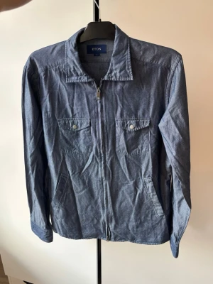 Jättefin Eton overshirt M - Supersnygg populär och eftertraktad Eton overshirt i tunt jeans material och storlek M. Grym passform och perfekt nu till hösten! Använt men super bra skick! Tveka inte vid minsta fråga 