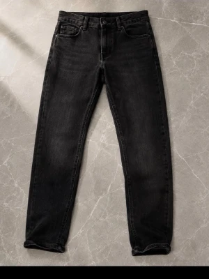 Svarta raka jeans med fem fickor - Snygga svarta jeans med rak passform och klassisk femficksdesign. Jeansen har subtila slitningar och en mörk tvätt som ger en cool look. Tillverkade i denim med bälteshällor och knappgylf. Perfekta för en avslappnad stil.