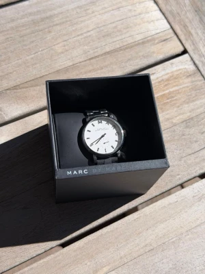 Marc Jacobs klocka  - Marc Jacobs MBM3242 Klocka kombinerar en ren vit urtavla med ett armband i rostfritt stål för minimalistisk, vardaglig elegans. Dess kvartsurverk och 5 ATM vattentålighet gör den praktisk såväl som stilfull. Sparsamt använd, inga skador. Orginalbox + extradelar till länk ingår. 