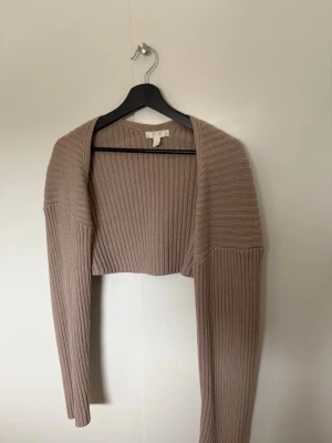 Beige ribbstickad bolero - Trendig beige ribbstickad bolero med lång ärm och öppen front. Materialet är mjukt och stretchigt för extra komfort. Färgen syns bäst på bild 3. Passar xs-m
