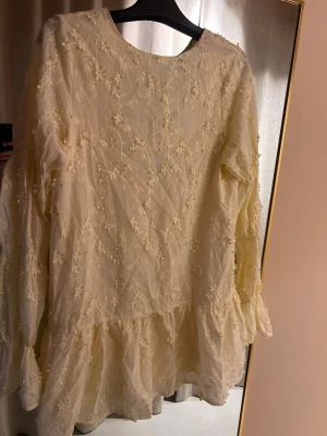 Gul blommig klänning från NA-KD - Söt gul kortklänning från NA-KD med broderade blommor och volang nedtill. Klänningen har långärmade ärmar och rund halsringning. Den är urringad i ryggen. Perfekt för sommarens alla tillfällen. Pris kan diskuteras.