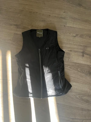 Svart dunväst från Pinewood S/M - Snygg svart dunväst från Pinewood med dragkedja framtill och två praktiska fickor med dragkedja. Västen har en stilren design med diskret Pinewood-logga på bröstet. Perfekt för lager-på-lager och håller dig varm under kyliga dagar.