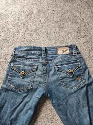 Lågmidjade vintage jeans  - Snygga lågmidjade bootcut vintage jeans. Kedjan har gått sönder men har lagat den och den går fortfarande att använda, och övriga fel är lagade. Köpte för ca 700. Längden passar mig bra som är 170 cm.  Mått: Midja (rakt över): 38  Innerbenslängd: 82 Yttre ben längd:98 