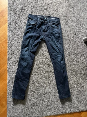 Mörkblå Replay Hyperflex jeans - Snygga mörkblå slim fit jeans från Replay, modell Anbass Hyperflex. Jeansen har klassisk femficksdesign, stretchigt material och normal midja. Perfekta för dig som gillar en smalare passform och vill ha bekväma jeans med mycket rörelsefrihet.