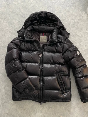 Svart moncler maya jacka  - Väldigt snygg och eftertraktad Moncler Maya jacka. Storlek M. Nypris ca 10 000+ kr. Jackan är i bra skick! Varm och skön med dunfyllning, perfekt för alla dagar. Tar bara bud.