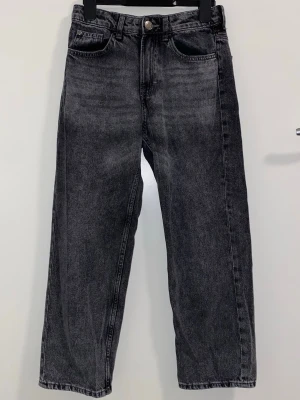 Svarta raka jeans med tvättad look - Säljer ett par svarta jeans med tvättad, lite blekt finish och raka ben. Klassisk femficksmodell med knapp och dragkedja framtill. Jeansen har en avslappnad passform och är perfekta för en cool vardagsstil.
