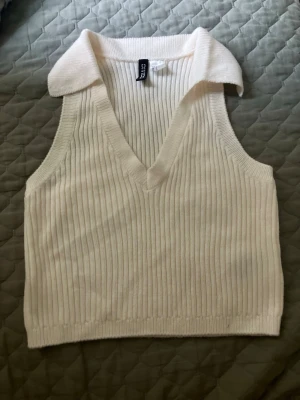 Cream vit ribbad ärmlös linnetopp - Säljer en vit ribbad linnetopp med krage och djup v-ringning. Toppen är ärmlös och har en croppad passform som passar perfekt till jeans eller kjol. Materialet känns mjukt och stretchigt, vilket gör den bekväm att bära hela dagen.
