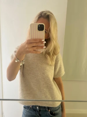 Beige stickad t-shirt - Mysig beige stickad t-shirt med korta ärmar och rund hals. Perfekt till jeans eller kjol för en avslappnad men ändå stilren look. Materialet känns mjukt och har en lätt luddig yta. .