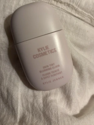 Kylie Cosmetics Skin Tint Foundation 1N - Foundation från Kylie Cosmetics i nyansen 1N. Kommer i en ljuslila, oval plastflaska med skruvlock. Produkten heter Skin Tint Blurring Elixir och ger en naturlig finish. Innehåller 30 ml och är enkel att ta med i väskan.