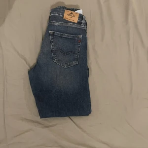 Replay Thad blå jeans straight fit - Snygga blå jeans från Replay, modell Thad. Klassisk femficksdesign med raka ben och normal passform. Jeansen har en mörk tvätt med lätt slitning och tydliga sömmar. Perfekta för dig som gillar en enkel och stilren look.