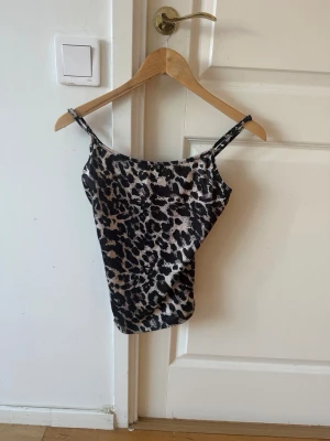 Leopardmönstrad linnetopp - Säljer en leopardmönstrad linnetopp med tunna axelband. Toppen har en beige och svart färgkombination och är ärmlös. Materialet känns som polyester eller syntet, vilket ger ett mjukt och följsamt fall. Perfekt för dig som vill sticka ut lite extra.
