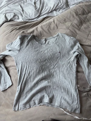 Ljusgrå långärmad topp - En enkel och stilren ljusgrå långärmad topp i mjukt material. Rund halsringning och diskret liten logga på bröstet. Perfekt att matcha med jeans eller kjol för en avslappnad look.