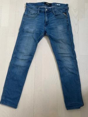 Replay jeans - Snygga blå jeans från Replay med raka ben och klassisk femficksmodell. Jeansen har diskreta slitningar och ljusare partier framtill för en trendig look. Tillverkade i mjukt denimtyg som sitter skönt hela dagen. Storlek W30 L29