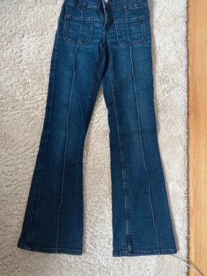 Mörkblå bootcut jeans med fickor storlek 158 - Snygga mörkblå jeans med bootcut passform och markerade sömmar framtill. Jeansen har stora fyrkantiga fickor fram och klassiska bakfickor. Tillverkade i denim med lätt stretch för skön känsla. Perfekta för en trendig och avslappnad stil. storlek 158