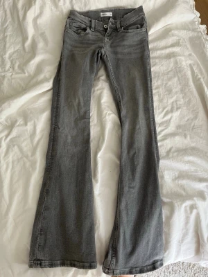 Grå bootcut jeans med broderade fickor - Säljer ett par grå bootcut jeans med snygga broderade detaljer på bakfickorna. Jeansen har klassisk femficksmodell, normal midja och utsvängda ben. Perfekta för dig som gillar en retroinspirerad look och vill ha något som sticker ut lite extra.