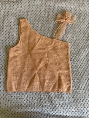 Aprikosfärgad topp med rosett - Säljer en somrig aprikosfärgad topp från Zara med en stor rosett i mesh på axeln, har ett diskret blommönster i tyget och är croppad i modellen. Storlek 152 men fungerar som XXS/XS. Aldrig använd, bara provad. 