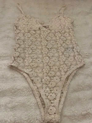 Krämvit spetsbody från H&M XS - Söt krämvit body från H&M i storlek XS. Bodyn är gjord i virkad spets med blommönster och har tunna axelband. Perfekt för dig som gillar romantisk och feminin stil. Materialet är mjukt och stretchigt för en bekväm passform.