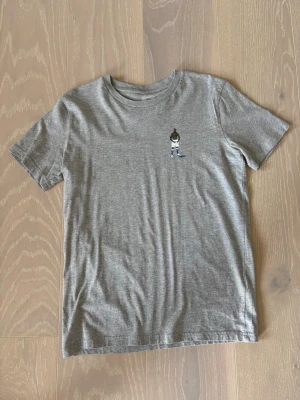 Grå t-shirt med tryck av fotbollsspelare - Snygg grå t-shirt i bomull med ett litet tryck av Mario Balotelli på bröstet. T-shirten har rund hals och korta ärmar, perfekt för en avslappnad stil. Passar dig som gillar sportiga detaljer och enkel design. Vid intresse eller frågor är det bara att höra av sig 