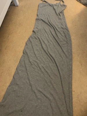 Grå långklänning med smala axelband - Långklänning i mjukt grått tyg med smala axelband och enkel, rak passform. Perfekt för varma dagar och enkel att styla med accessoarer. Tunn och bekväm, passar till många tillfällen.