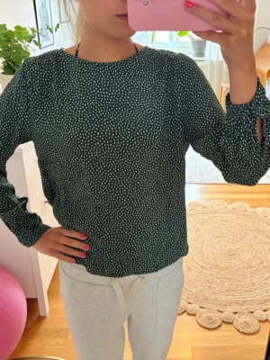 Mörkgrön prickig blus - Fin mörkgrön blus med vita prickar. Blusen har långa ärmar med knappdetalj vid ärmslut och i nacken. Kontakta om du har frågor💗