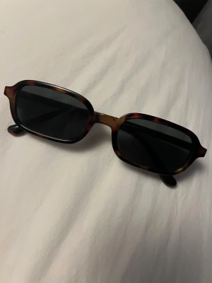 Såååå snygga trendiga glasögon!!!! - Snygga solglasögon med rektangulära bågar i brunsköldpaddmönster och mörka linser. Klassisk och trendig look som passar perfekt till sommaren. Bågarna har en lätt glansig finish och ger en cool vintage vibe. Köpte dessa för bara någon månad sedan! Säljer pga använder inte så mycket!  Nyskick!!! Lite mörkgrönt/svart glas! Med brun/leopard bågar! Priset kan absolut diskuteras🥰 Postar snabbt