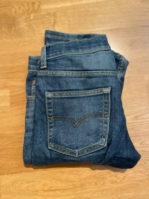 Mörkblå slim fit jeans från Levi - Snygga mörkblå jeans i slim fit-modell med klassiska fickor och kontrastsömmar. Jeansen har en enkel design och är tillverkade i denim med lätt stretch för skön passform. Perfekta för en avslappnad och trendig stil.