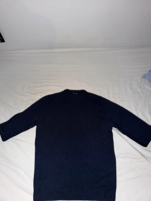 Mörkblå stickad tröja unisex - En enkel och stilren mörkblå stickad tröja med rund hals och långa ärmar. Tröjan har en rak passform och ribbade muddar vid ärmslut och nederkant. Perfekt att matcha med jeans eller kjol för en clean look.