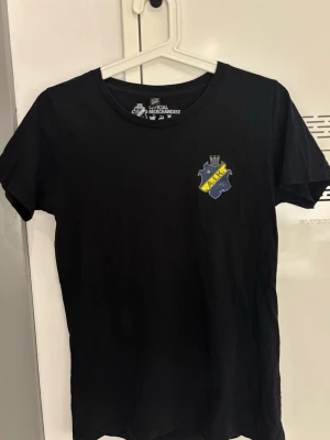 Svart AIK t-shirt med tryck - Svart t-shirt med AIK:s klubbmärke tryckt på bröstet. Klassisk rund halsringning och korta ärmar. Perfekt för dig som vill visa ditt AIK-stöd på ett stilrent sätt 🩷
