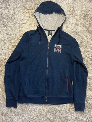 Helly Hansen Zip hoodie - Säljer denna riktigt snygga marinblå zip hoodie från Helly Hansen. Den är i bra skick utan defekter och är i storlek s. Bara att skriva över frågor och funderingar.