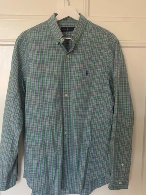 Grönrutig skjorta från Ralph Lauren - Säljer en klassisk grönrutig skjorta från Ralph Lauren i bomull. Skjortan har lång ärm, knappar framtill och button-down krage. Den har blå broderad logga på bröstet och passar perfekt till en avslappnad men ändå stilsäker look.