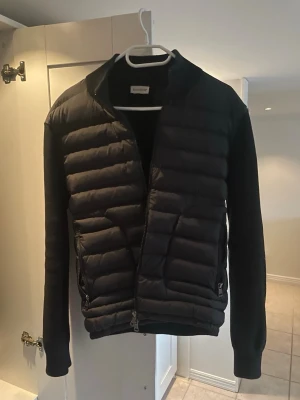 Moncler Cardigan - Snygg svart Moncler jacka. Perfekt för kalla dagar och ger en modern look. Materialet är en mix av vadderad polyester och stickat tyg. Dessa jackorna är väldigt små i storlek. Sitter mer som en S. Jag är 174 och den är på gränsen till för liten. Beror lite på hur du vill passformen ska vara.