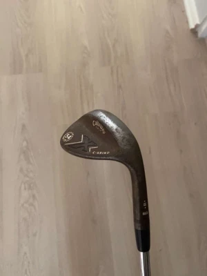 Golfklubba callaway - Golfklubba Callaway Mack Daddy 54° wedge med C-Grind. Klubban har ett brunt klubbhuvud i metall och ett skaft i krom med svart grepp. Perfekt för närspel och bunkerslag på golfbanan.