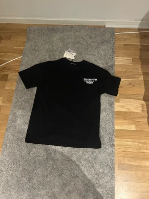 Svart t-shirt från Cole Buxton - Svart t-shirt från Cole Buxton med vit text på bröstet. Klassisk passform och rund halsringning. Tillverkad i mjuk bomull som känns skön mot huden. Perfekt för dig som gillar stilrena och enkla plagg med en modern touch.