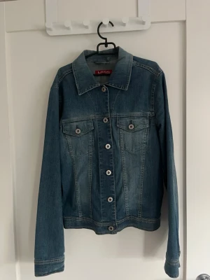 Klassisk blå jeansjacka - Snygg blå jeansjacka med raka ärmar och knappar framtill. Två bröstfickor med lock och knapp, samt klassisk krage. Jackan har en tidlös design och passar perfekt till många olika stilar. Det är bara att skriva om det finns någon fråga! Priset kan diskuteras.💕