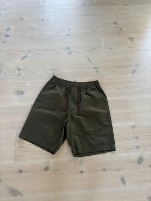 Mörkgröna linneshorts Uniqlo - Snygga mörkgröna shorts med avslappnad passform och elastisk midja. Shortsen har två sidofickor fram och en bakficka. Perfekta för varma dagar och enkla att matcha med olika stilar.