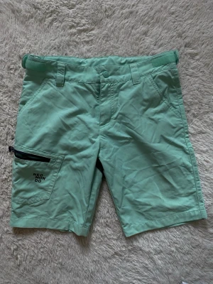 Mintgröna shorts från Neomondo - Mintgröna funktionsshorts från Neomondo med svart detalj baktill och dragkedjeförsedd ficka på sidan. Shorts med bälteshällor, knappstängning och praktiska fickor. Perfekta för utomhusaktiviteter och äventyr.