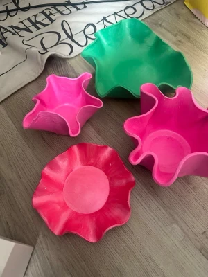 Färgglada vågiga skålar i lera  - Fyra dekorativa skålar med vågig form, tre i olika nyanser av rosa och en i grön. Perfekta som inredningsdetaljer eller förvaring av småsaker. Skålarna har en unik, blomliknande design och är lätta att placera ut i hemmet. 50kr för alla 