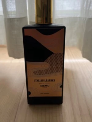 Italian Leather parfym från Memo Paris! - Säljer en lyxig parfymflaska från Memo med doften Italian Leather. Flaskan är svart med en elegant guld- och svart etikett och har ett guldfärgat lock. Designen är modern och stilren, perfekt för dig som gillar exklusiva dofter och snygga flaskor i badrumshyllan.