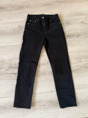 Arket Svarta raka jeans, storlek 25 - Snygga svarta jeans med rak passform och klassisk femficksdesign. Jeansen har knapp- och dragkedjestängning samt silverfärgade nitar. Perfekta till en avslappnad stil och passar till det mesta i garderoben. Använda 1 gång! .