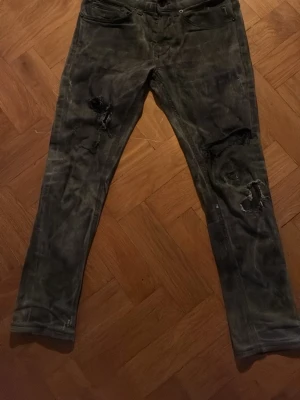 Dondup Grå slitna jeans med hål - Säljer ett par grå Dondup jeans med slitningar och hål på båda benen. Jeansen har en smal passform och klassisk femficksdesign. Perfekta för dig som gillar en edgy och avslappnad stil.