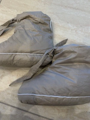 Grå tofflor med knytband Georg Jensen - CLOUD DOWN SOCK  Bløde og lune andedunsokker med elegant piping og bindebånd ved anklen. Cloud dunsokkerne er satinvævet i 100 % bomuld med fyld af luftige og åndbare andedun og fjer. Farven Cashmere er en brun nuance af grå med et roligt og eksklusivt udtryk.  Str M (36-40)  Næsten ikke brugt.. 