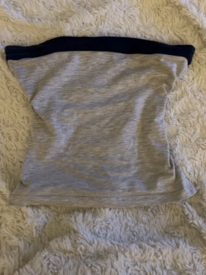 Grå tubtopp från Subdued - Säljer en enkel och stilren grå tubtopp från Subdued med mörkblå kant upptill. Perfekt att matcha med jeans eller kjol för en clean look. Mjuk och stretchig känsla som sitter snyggt på kroppen.