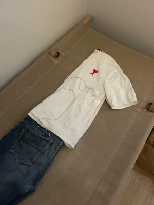 AMI PARIS T-shirt  - AMI PARIS t-shirt i bomull med rund hals och korta ärmar. På bröstet finns ett broderat rött hjärta med bokstaven A. Enkel och stilren design som passar till det mesta.