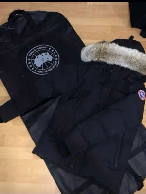 Svart Canada Goose parkas med päls - Säljer en svart parkas från Canada Goose med äkta päls på huvan och klassisk logga på ärmen. Jackan har dragkedja och knappar framtill samt flera fickor. Perfekt för kalla vinterdagar och riktigt snygg streetstil.