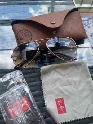 Ray-Ban aviator solglasögon guld - Snygga Ray-Ban aviator solglasögon med guldfärgad metallbåge och mörka tonade glas. Kommer med originalfodral, putsduk och tag. Klassisk pilotmodell som ger en tidlös look.