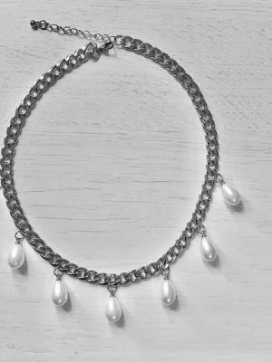 Kedjehalsband med droppformade pärlor - Snyggt halsband med grov silverfärgad kedja och fem droppformade vita pärlor som hänger längs kedjan. Justerbar längd med förlängningskedja. Perfekt för att ge en cool touch till din outfit.