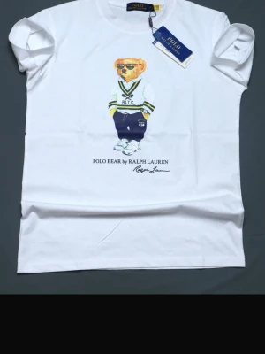 Vit Polo Bear t-shirt från Ralph Lauren - Vit t-shirt från Ralph Lauren med Polo Bear-tryck framtill. Klassisk rund hals och korta ärmar. T-shirten är i mjuk bomull och har en avslappnad passform. Perfekt för dig som gillar ikoniska prints och stilren design.
