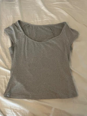 Grå croppad topp med kort ärm - Snygg grå topp med croppad passform och korta ärmar. Tillverkad i mjukt material som känns skönt mot huden. Perfekt till jeans eller kjol för en enkel och clean look.