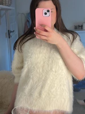 Vit fluffig stickad tröja - Säljer en supermjuk och fluffig vit stickad tröja med kortare ärmar och avslappnad passform. Perfekt för dig som gillar mysiga och trendiga plagg. Materialet känns lurvigt och ger en cool look.storlek L men sitter som en xs. 