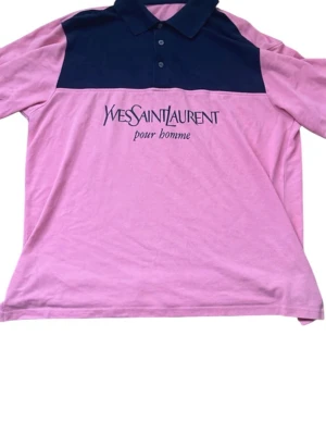 Rosa och marinblå YSL pikéskjorta - Säljer en rosa och marinblå pikéskjorta från Yves Saint Laurent med tryckt logga på bröstet. Skjortan har krage, knappar framtill och lång ärm. Perfekt för dig som vill ha en unik och stilren look.